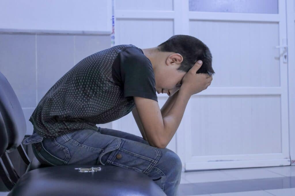 A young person sitting alone on a chair with head in hands, cast in heavy shadow, symbolizing the psychological impact of Adverse Childhood Experiences and trauma.